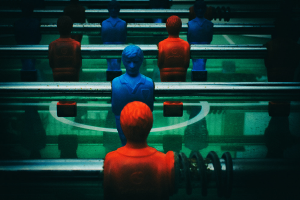 Ein bunt bemalter Tischfussball mit einer Gruppe von Menschen in verschiedenenfarbigen Trikots, positioniert in der Mitte des Tisches, bereit für ein Spiel von Tischfussball.