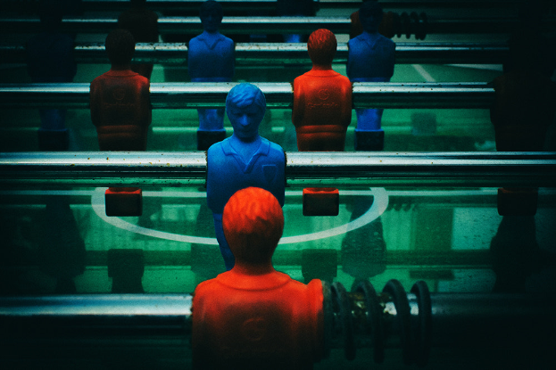 Ein bunt bemalter Tischfussball mit einer Gruppe von Menschen in verschiedenenfarbigen Trikots, positioniert in der Mitte des Tisches, bereit für ein Spiel von Tischfussball.