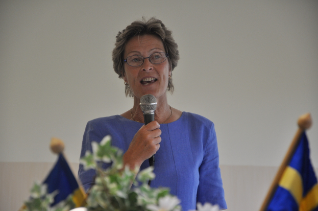 Eine Frau steht an einem Podium mit zwei Flaggen dahinter und spricht in ein Mikrofon.