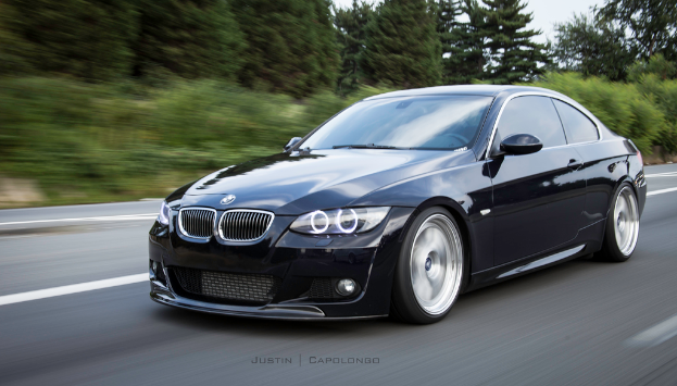 Ein schwarzer BMW f├Ąhrt auf einer Stra├če mit B├Ąumen im Hintergrund.