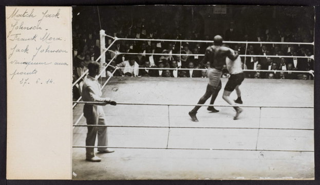 Schwarz-weiß-Foto von zwei Boxern im Ring, einem Schiedsrichter links daneben und Zuschauern im Hintergrund, mit dem Text "Jack Johnson vs Frank Morgan" oben links.