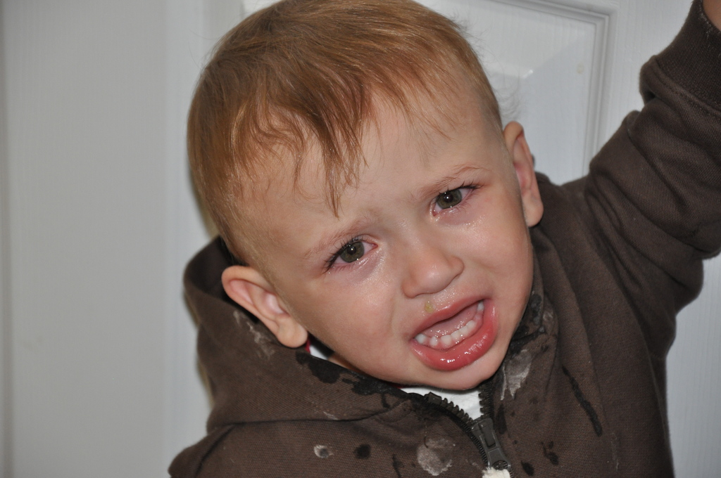 Ein kleiner Junge weint vor einer weißen Wand mit einer Tür im Hintergrund.