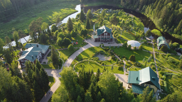 Luftaufnahme eines Resorts inmitten eines dichten Waldes mit Gebäuden, Straßen und einem Fluss in der Mitte, unter einem klaren Himmel.