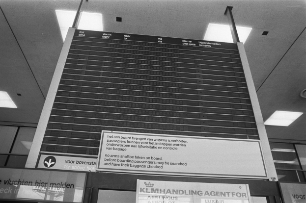 Ein Schwarz-Weiß-Foto eines Abflugsbildschirms an der Decke, der von Lampen beleuchtet wird.