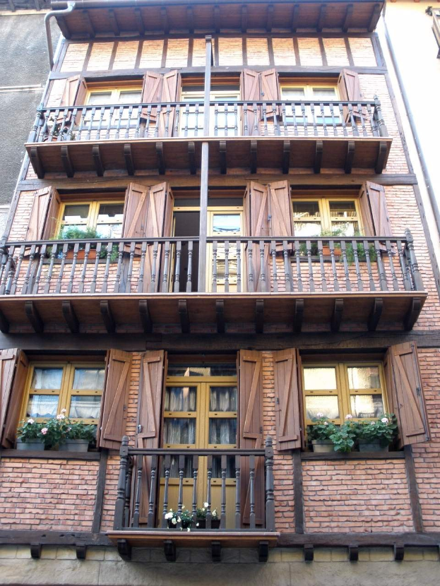 Ein mehrstöckiges Gebäude in Straßburg, Frankreich, mit zahlreichen Fenstern, Balkonen, Geländern, Türen und Blumentöpfen mit Pflanzen.