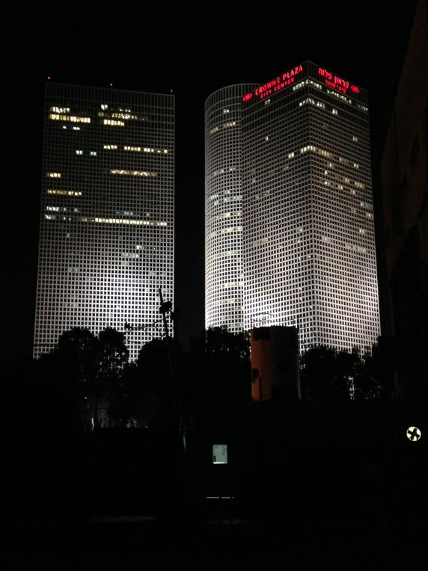 Eine spärliche Landschaft mit einigen Bäumen im Vordergrund und mehreren Gebäuden im Hintergrund.