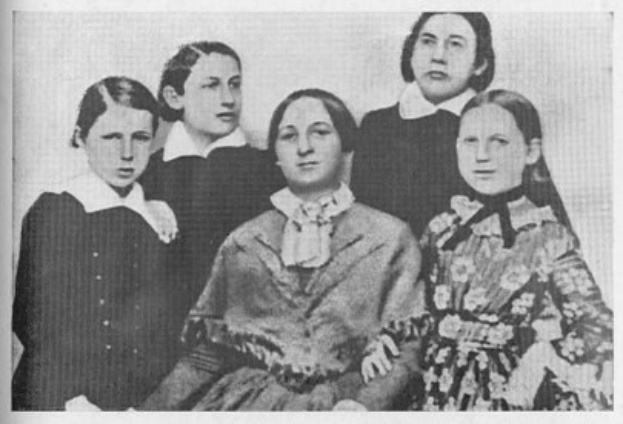 Schwarzes und weißes Foto einer Gruppe von Frauen aus der Frauenwahlrechtsbewegung, mit einer Frau in der Mitte sitzend und anderen Frauen um sie herumstehend.