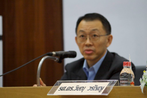 Eine Person in einem Anzug sitzt auf einem Stuhl und spricht in ein Mikrofon.