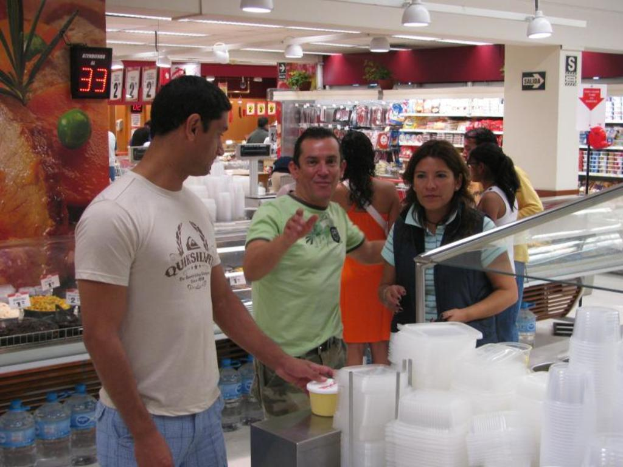 Eine Gruppe von Menschen steht in einem Einkaufsladen mit Lebensmitteln auf den Regalen und Lampen an der Decke.