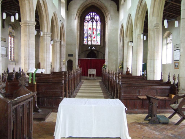 Ein Raum mit Tischen, einem Podium, einem Buchständer, Stühlen, Bänken, Säulen, Tafeln, einem Vorhang, Fenstern, Tüchern, Pflanzen und diversen Gegenständen.
