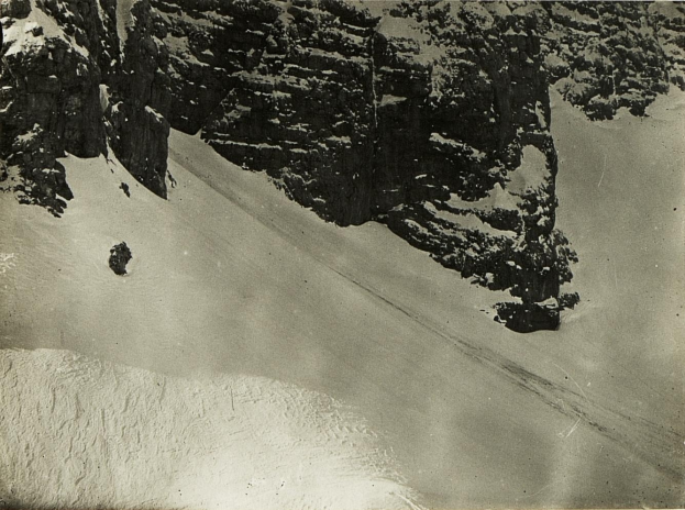 Eine Person, die eine schneebedeckte Berglandschaft hinabskifährt, umgeben von schneebedeckten Hügeln, mit Text am unteren Bildrand.
