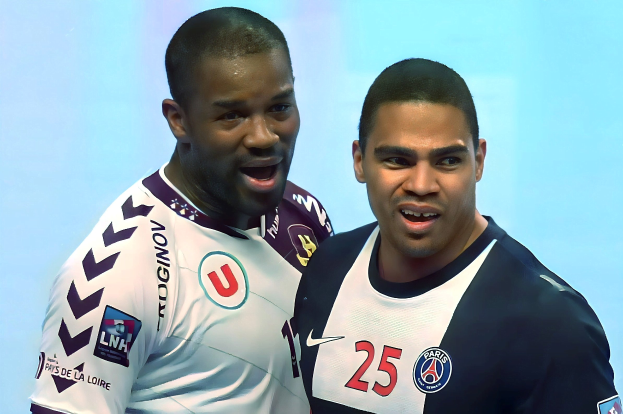 Zwei Männer in weißen und blauen Fußballtrikots stehen auf einem Feld und feiern mit erhobenen Armen.