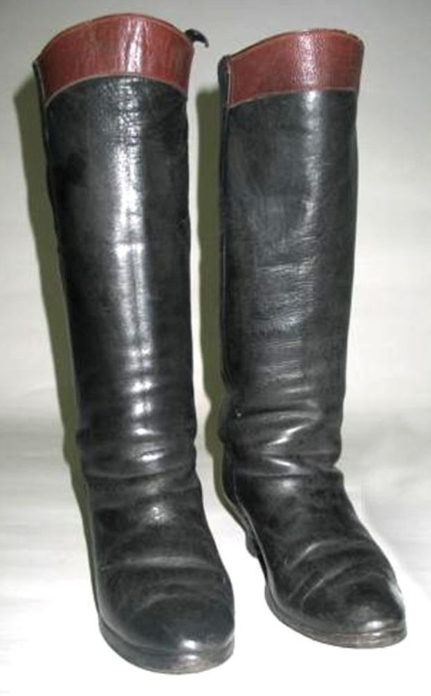 Schwarze Stiefel mit roten Schnürsenkeln und Sohlen auf einer weißen Oberfläche, mit einem glänzenden Lederobermaterial, gerundeter Zehe und niedriger Absatz.