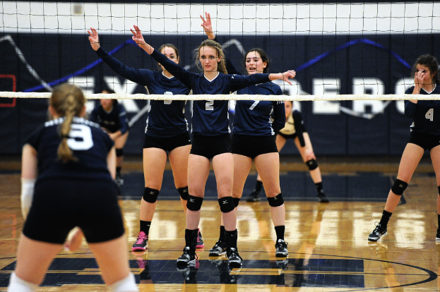Drei Mädels bei einem Volleyballspiel auf dem Feld stehend, ein Netz davor und ein Zaun im Hintergrund.