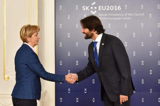Bundeskanzlerin Angela Merkel und Bundeskanzlerin Joachim Gauck schütteln Hände vor einem 'EU-Gipfel'-Plakat, freundlich und einladend lächelnd.