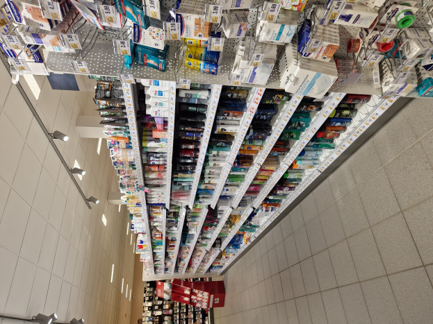 Eine Apothekenregal mit verschiedenen Medikamenten in Gestellen, beleuchtet von Deckenlampen.