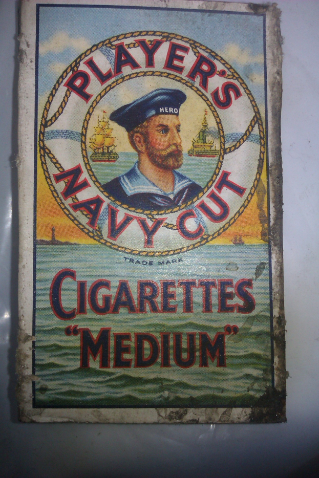 Plakat mit einer Person in einer marineblauen Uniform mit weißem Hemd und roter Krawatte, die Arme verschränkt und einen strengen Gesichtsausdruck hat, bewirbt "Player's Navy Cut Cigarettes Medium" in fetter schwarzer Schrift innerhalb einer weißen Grenze.