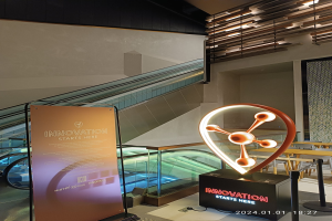 Großes Schild in der Mitte eines Gebäudes mit einer Rolltreppe im Hintergrund, Tische und Stühle auf der rechten Seite und eine Tafel mit "Innovation beginnt hier" auf der linken Seite, die auf die HSTP20 Expo hinweist.