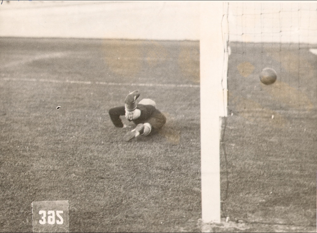 Ein Schwarz-Weiß-Foto eines Fussballspielers, der einen Ball vor einem Torpfosten mit Netz auf der rechten Seite fängt, mit Text unten.