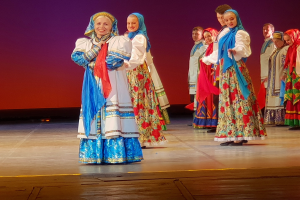 Eine Gruppe von Menschen in farbenfrohen, detaillierten traditionellen ukrainischen Kostümen, die auf einer Bühne lächeln und stehen.