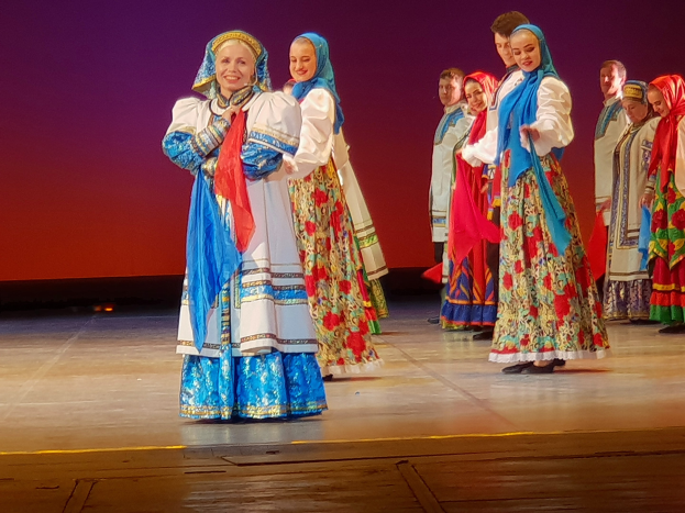 Eine Gruppe von Menschen in farbenfrohen, detaillierten traditionellen ukrainischen Kostümen, die auf einer Bühne lächeln und stehen.