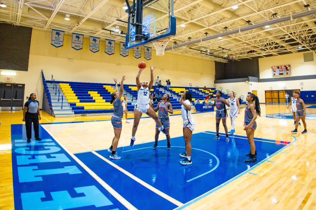 Eine Gruppe von Frauen, die Basketball in einer Turnhalle spielen, mit einem Scoreboard, das ihren NCAA-Turniersieg anzeigt.