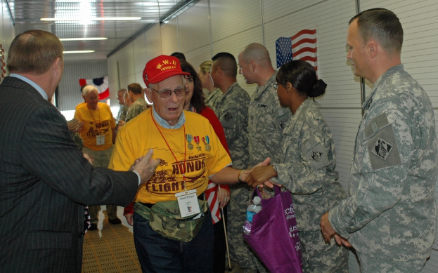 Eine Gruppe von Menschen und Soldaten steht drinnen mit einer Fahne auf der rechten Wand und Lampen an der Decke.