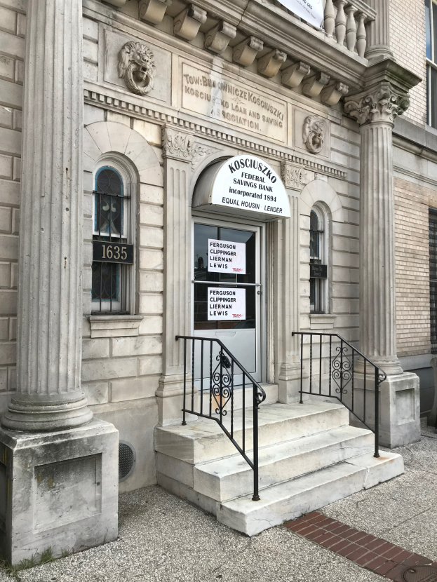 Außenansicht des Kosciuszko Federal Savings Bank-Gebäudes mit einem Schild, Fenstern, Säulen, einer Tür, einer Treppe mit Geländer und einer Fahne.