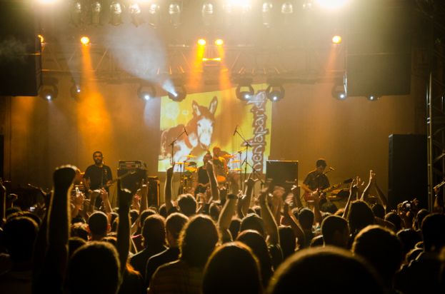 Eine Gruppe von Menschen mit einigen, die Musikinstrumente vor Mikrofonen spielen, während andere in der Nähe stehen, mit Lautsprechern, Lichtern und Metallstangen im Hintergrund.