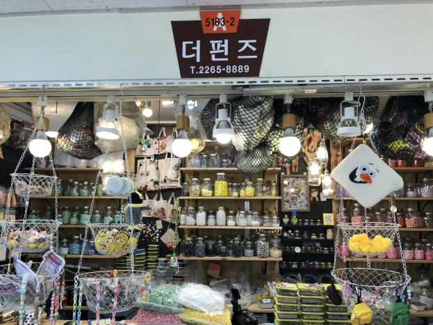 Ein unordentlicher Laden in Seoul mit verschiedenen Gegenst%C3%A4nden wie K%C3%B6rbchen, Lichtern, Flaschen und Spielzeugen, mit einer Tafel oben, die ihn als einen der besten koreanischen L%C3%A4den ausweist.
