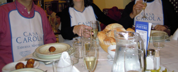 Personen sitzen an Tischen mit Tellern, Geschirr, Besteck, Brotkörben, Gläsern und einer Werbung.