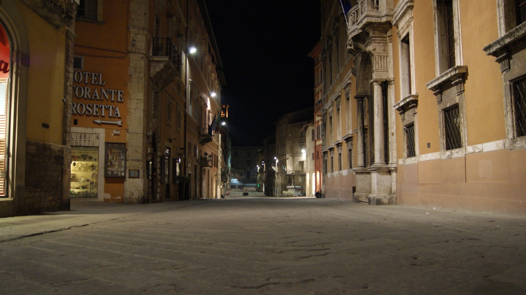 Eine nächtliche Straßenszene mit Gebäuden auf beiden Seiten und einem Geschäft auf der linken Seite sowie Lichtern in der Mitte.
