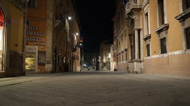 Eine nächtliche Straßenszene mit Gebäuden auf beiden Seiten und einem Geschäft auf der linken Seite sowie Lichtern in der Mitte.