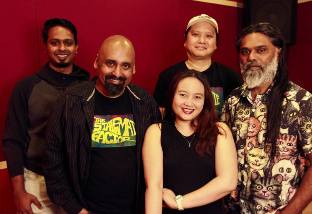 Eine Gruppe von Menschen, die in einem Aufnahmestudio zusammenstehen, lächeln und posieren für ein Foto vor einer roten Wand.