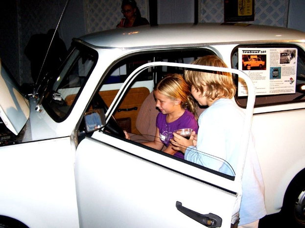 Zwei Kinder versuchen in ein Auto mit mehreren anderen Menschen in der Nähe einzusteigen.