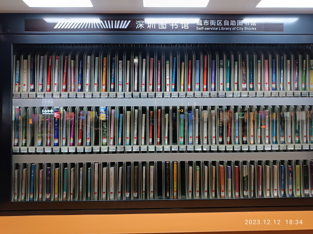 Eine gut beleuchtete Bibliothek mit hohen Bücherregalen voller Bücher, mit einer Tafel mit Text und einem Wasserzeichen unten, das an eine Selbstbedienungsbibliothek der Stadtblocks erinnert.