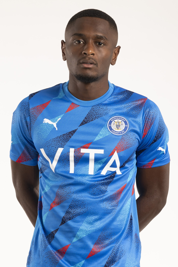 Ein Mann in einem blauen Leicester City Away-Shirt von der Saison 2018-19 steht mit Händen in den Taschen und einem leichten Lächeln da.