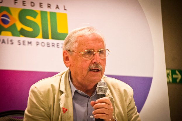 Eine Person, die in ein Mikrofon spricht und vor sich ein Banner mit der Aufschrift 'Bundes' hat.