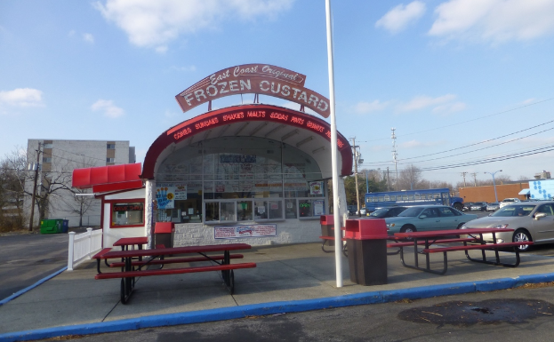 Eine Szene mit Autos, Pfählen, Gebäuden, Bänken, einem Schuppen mit einer Tafel und Plakaten auf dem Schuppen.