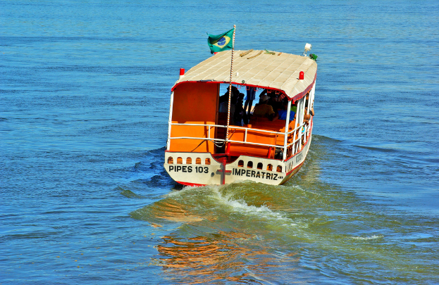 Ein Boot mit Menschen an Bord und einer Flagge mit Text, das auf dem Wasser segelt.