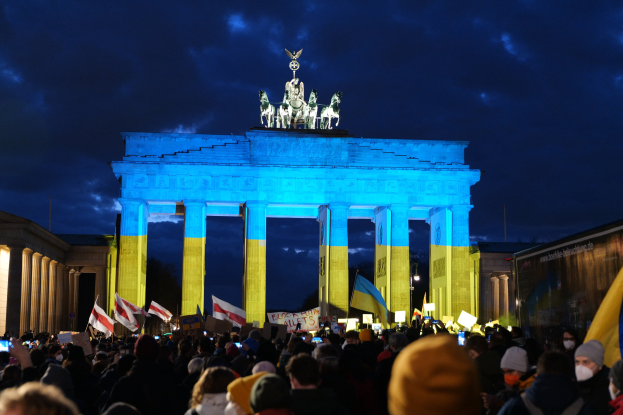 Eine Menschenmenge mit Fahnen und Plakaten steht vor dem Brandenburger Tor in Berlin, Deutschland, mit einer Schriftrolle auf der rechten Seite des Bildes.