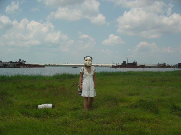 Eine Frau mit einer Plakette steht auf Gras mit Schiffen im Wasser dahinter.