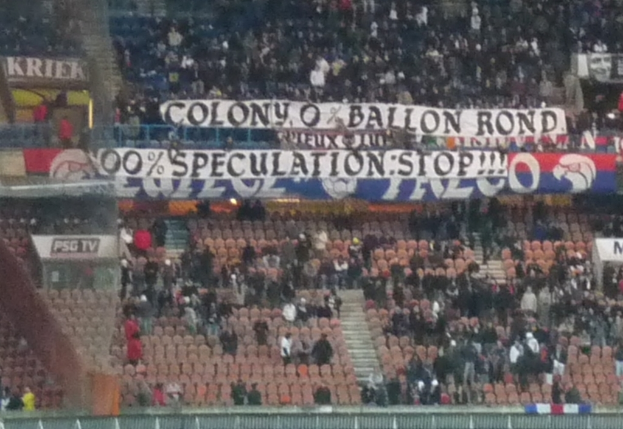 Ein Stadion voller großer Menschenmenge, Banner und Stühle, mit einem Zaun unten und Treppen auf der linken Seite.