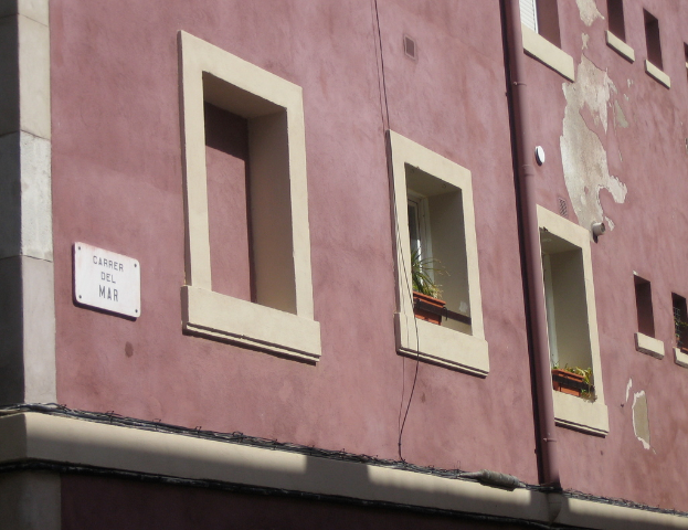 Ein Gebäude mit einem Namensschild, Rohren und Blumentöpfen auf den Balkonen.