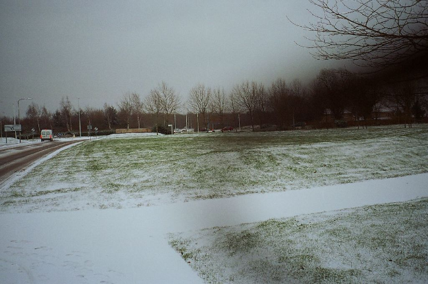 Eine schneebedeckte und nebelige Landschaft mit Fahrzeugen auf der Straße und Bäumen im Hintergrund.