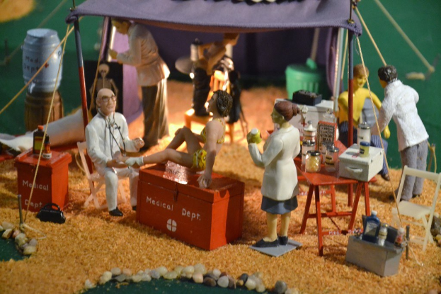 Eine Sammlung von Spielzeugen auf einem Tisch mit einer medizinisch thematischen Schachtel, einem violetten Zelt und verstreuten Gegenständen im Hintergrund.