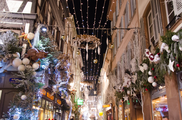 Ein lebhaftes Weihnachtsmarkt in Straßburg, Frankreich, mit Menschen, die zwischen Gebäuden mit Weihnachtsbäumen, Lichtern und anderen festlichen Dekorationen unter einem sichtbaren Himmel spazieren.