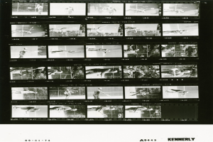 Schwarzes und weißes Foto eines konzentrierten Tennisspielers in einem weißen Hemd und Shorts, der einen Schläger hält, mit einem Filmstreifen-Hintergrund.