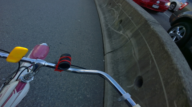 Ein Fahrradlenker unten, Fahrzeuge auf der Straße rechts und ein Teiler in der Mitte.