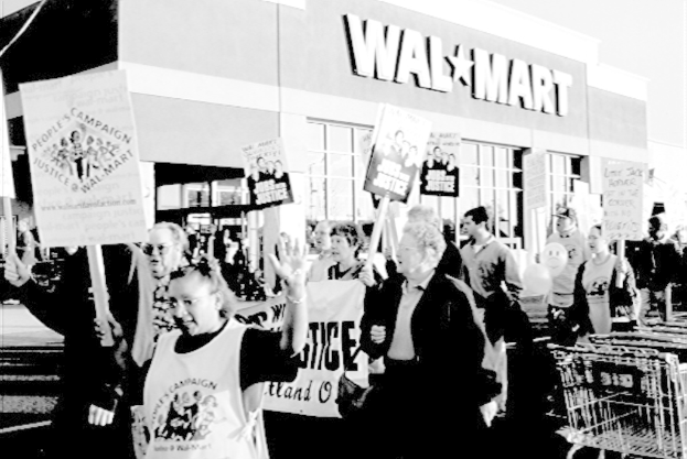Ein Schwarz-Weiß-Bild von Menschen, die vor einem Einkaufszentrum protestieren und Plakate halten.